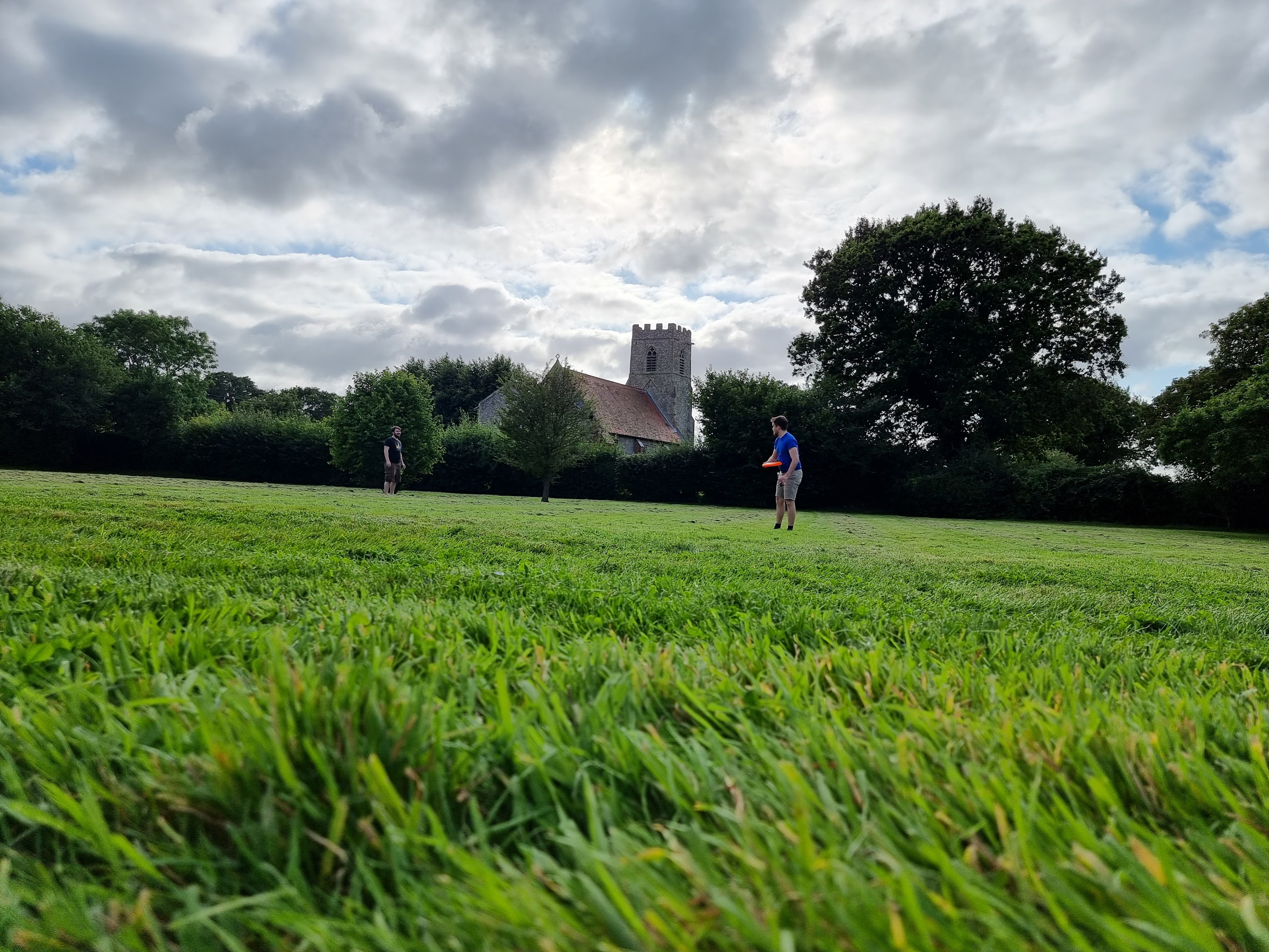 A photo of far away photo of my friends Ashley & Will throwing a frisbee around the garden